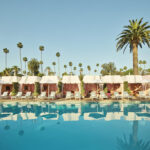 Piscine et cabanas du Beverly Hills Hotel à Los Angeles, avec palmiers, transats et décor rose et vert.