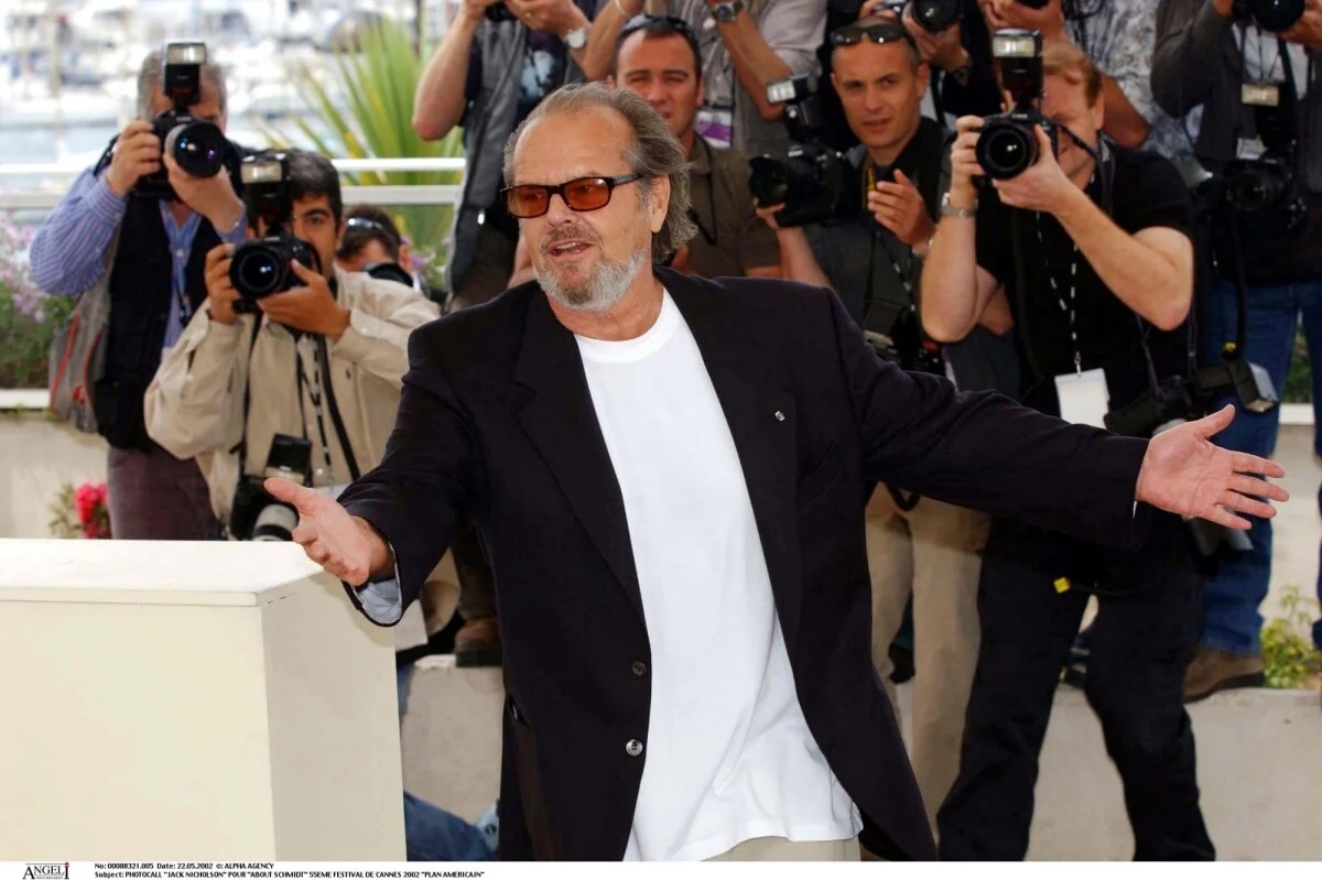 Jack Nicholson à Cannes en veste noire, tee shirt blanc et lunettes à verres rouges.
