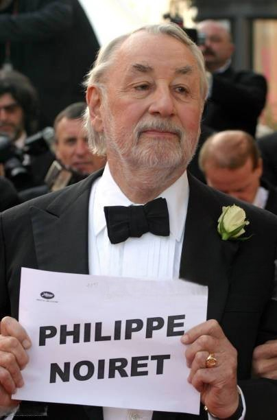 Philippe Noiret en smoking à Cannes, tenant une feuille portant son nom.