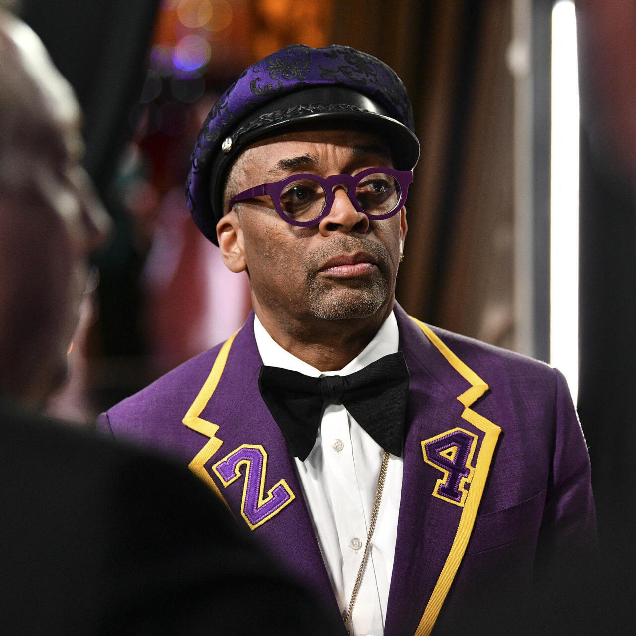 Spike Lee à Cannes dans une tenue violette et jaune, lunettes assorties et nœud papillon noir.