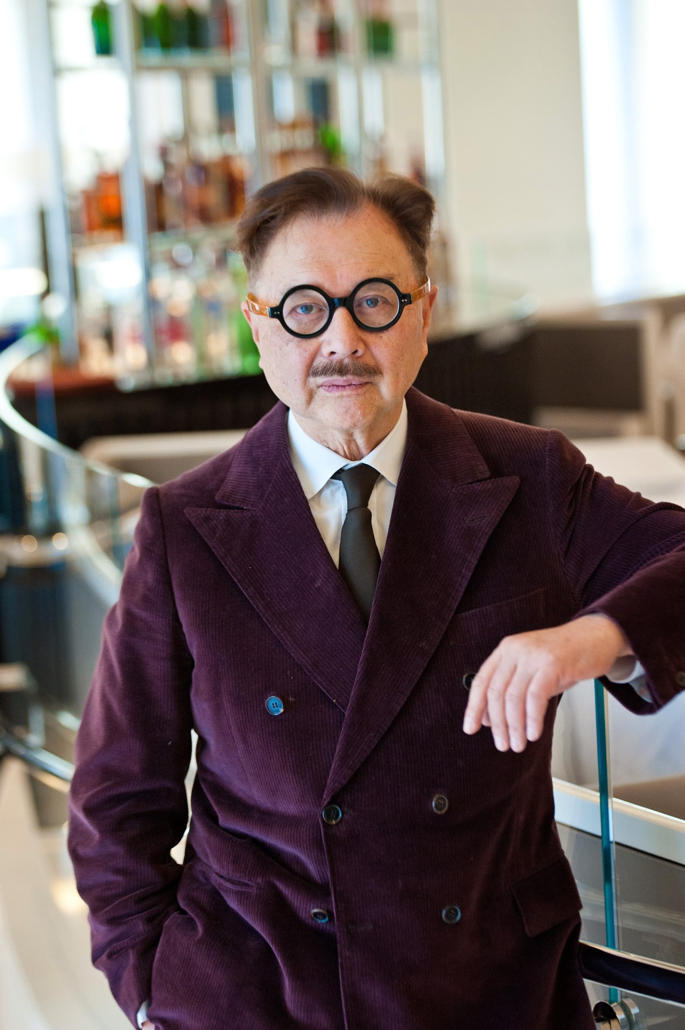Michael Chow en costume croisé aubergine et lunettes rondes.